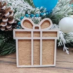 Free 3D layered laser cut wooden Christmas present ornament in a gingerbread style, displayed as a finished craft project on a rustic wooden table with snowy holiday branches and decorations.