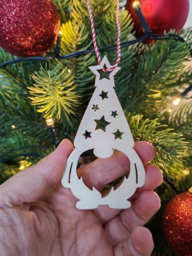 A hand holding a wooden Christmas gnome ornament cut with a laser machine, free SVG file for laser cutting.