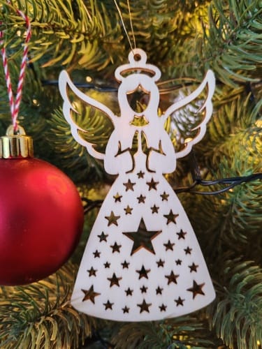 Finished wooden Christmas angel ornament with a starry dress pattern hanging on a Christmas tree next to a red bauble, made from a free SVG laser cut file.