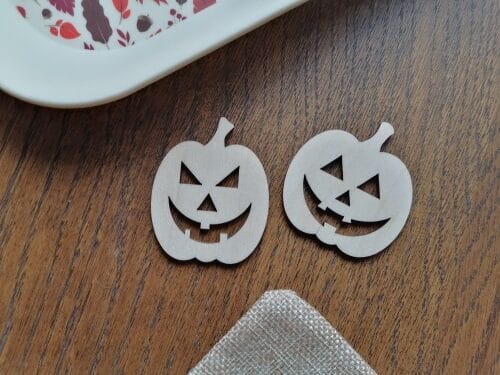 Two laser cut wooden Halloween pumpkin faces made from plywood sitting on a table, from a free Halloween pumpkin SVG set